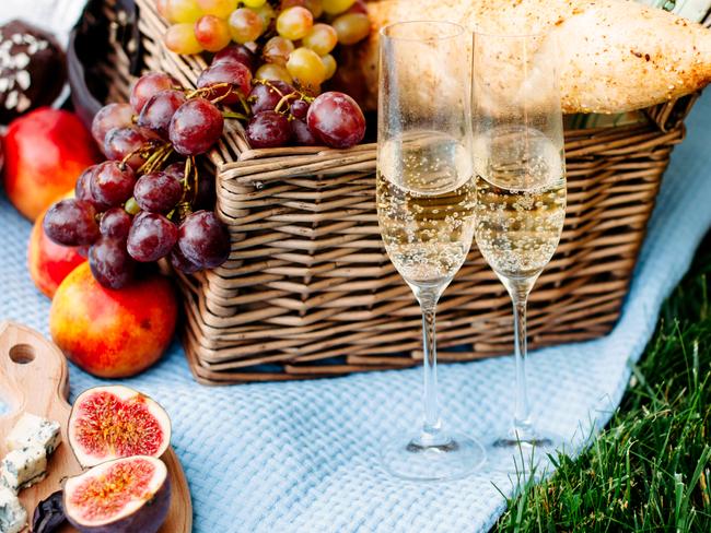 Picnic at the park on a grass, delicious food: basket, wine, grapes, peaches, baguette, cupcakes, figs, cheese, blue tablecloth, wineglass with champagne