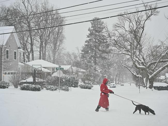 TOPSHOT - A pedestrian crosses the street as snow falls during a winter storm in Bethesda, Maryland on January 6, 2025. A massive storm system dumped heavy snow and freezing rain on large swaths of the eastern United States Monday, disrupting travel and work for millions of Americans from the Ohio Valley to the capital Washington. (Photo by PEDRO UGARTE / AFP)