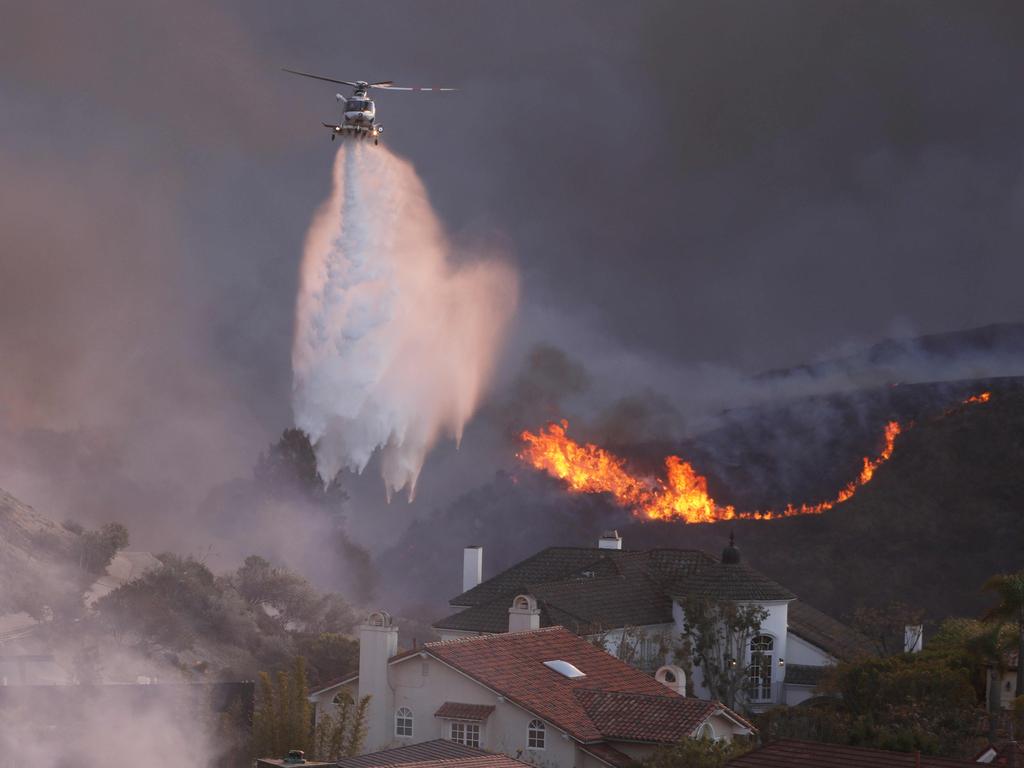 A helicopter drops water around homes threatened by the wind-driven Palisades Fire in Pacific Palisades, California, January 7, 2025. Picture: David Swanson / AFP.