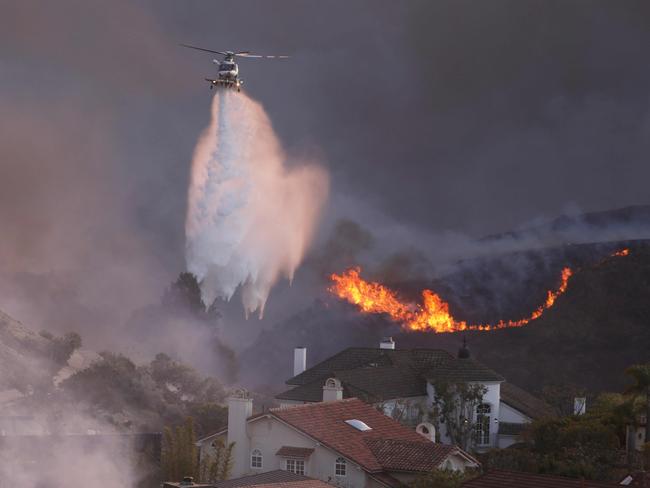 A helicopter drops water around homes threatened by the wind-driven Palisades fire in Pacific Palisades, California, January 7, 2025. Picture: David Swanson / AFP.