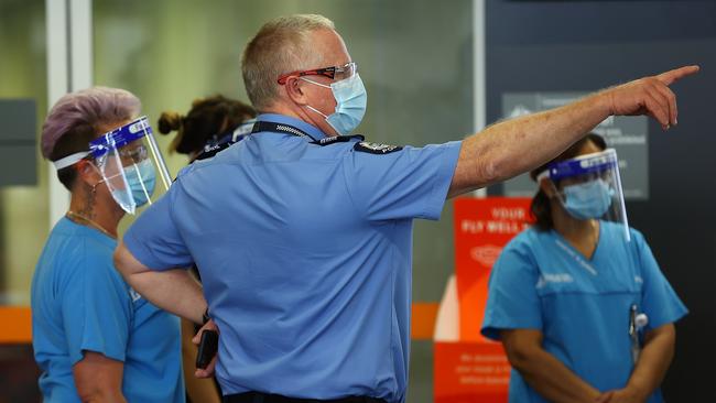 A police officer gestures as health care workers look on prior to passengers arriving from Brisbane on Qantas flight QF937 at Perth Airport on Saturday. Picture: Getty Images