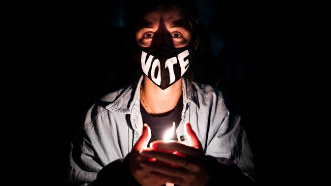 A woman wearing a face mask reading "vote" holds a candle as mourners gather on the steps of the Supreme Court.