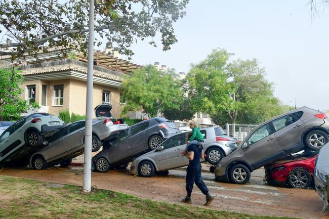 Pedestrians stand next to  piled up cars following deadly floods in Sedavi, south of Valencia