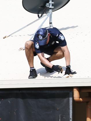 A police officer inspects the roof and gutter of the house where the children died. Pic: Brendan Radke