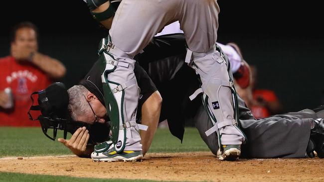 Umpire Paul Emmel falls to the ground as Stephen Vogt #21 of the Oakland Athletics rushes to his aid after being hit by the bat of Jefry Marte #19 of the Los Angeles Angels of Anaheim.