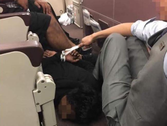 A Malaysia Airlines steward sits with a hogtied passenger who allegedly threatened to blow up the plane.