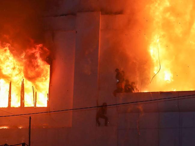 Fire burns around people on a ledge on the side of the Grand Diamond City hotel-casino in Poipet on December 29, 2022. Picture: AFP.