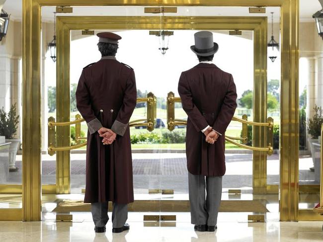 Concierge and bellboy standing at hotel entrance, rear view