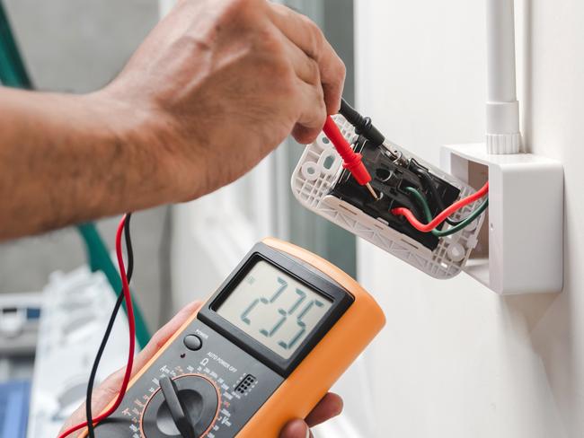 Electrician is using a digital meter to measure the voltage at the power outlet in on the wall.