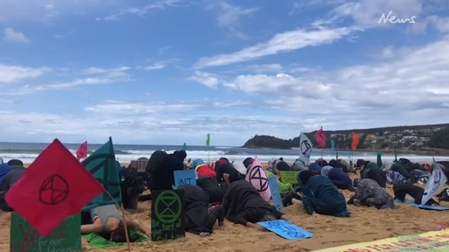 Extinction Rebellion protesters bury their heads in the sand on Manly Beach