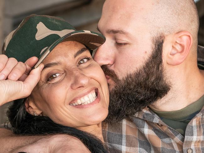 Caucasian couple of farmers in casual clothing hugging and smiling in large cow farm