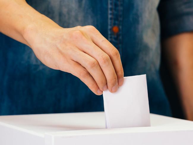 Front view of person holding ballot paper casting vote at a polling station for election vote in black background