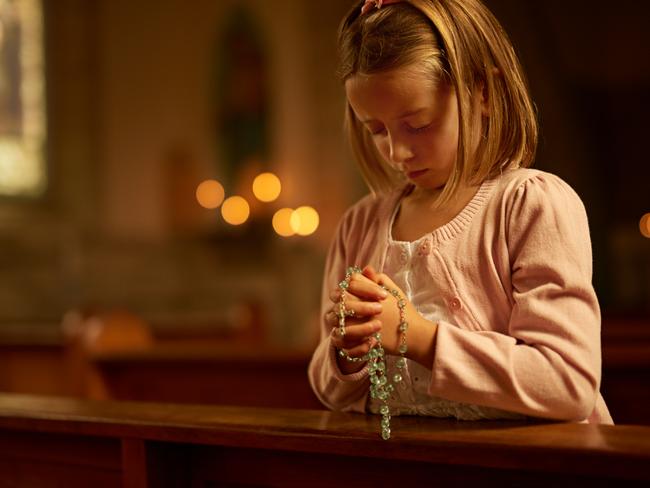 Cropped shot of a little girl praying while holding a rosary in church. istock image