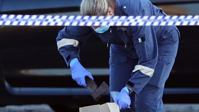 A forensic officer picks up a hatchet at the scene. Picture: David Crosling