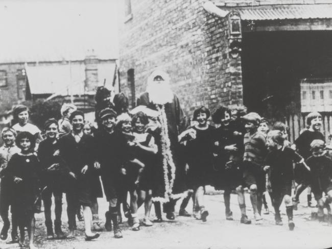 Father Christmas and children walking down a street in the 1930s. Picture: F. Oswald Barnett collection, State Library of Victoria