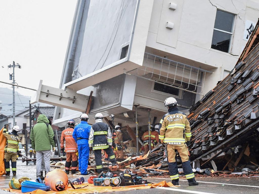 Firefighters work at the scene where a multi-storey building toppled over and crushed a house in the city of Wajima. Picture: AFP