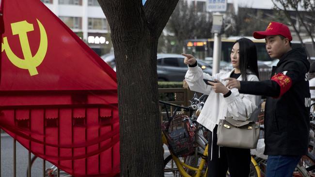 A volunteer gives directions to a resident near a Chinese Community Party flag on the streets of Beijing.