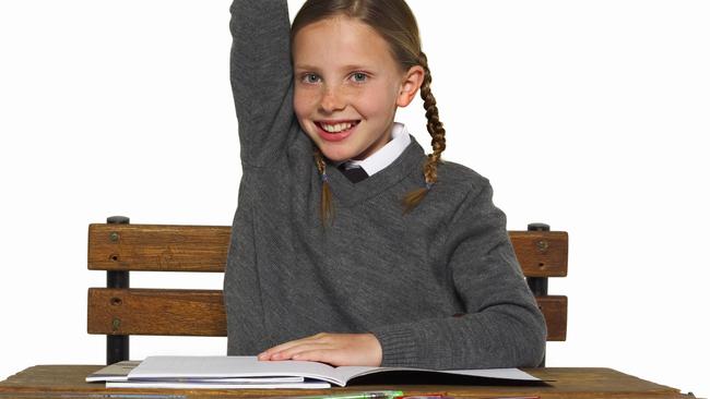 portrait of a schoolgirl (10-12) wearing a school uniform sitting at her desk raising her hand