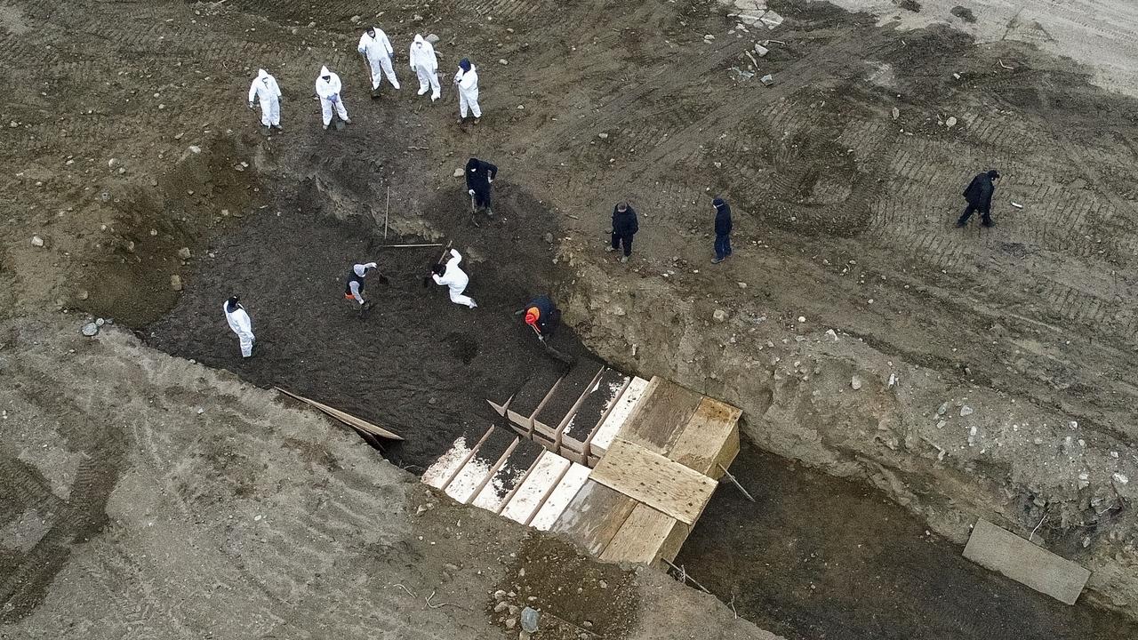 Workers wearing personal protective equipment bury bodies in a trench on Hart Island. (AP Photo/John Minchillo)