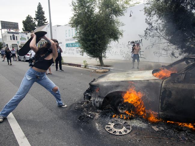 A woman uses a skateboard to batter a burning police vehicle in Los Angeles. Picture: AP