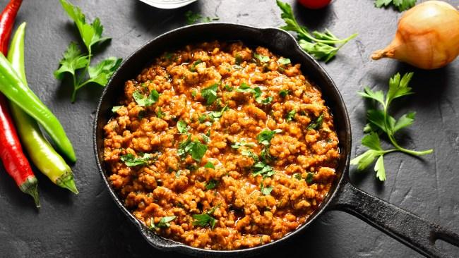 Keema curry in cast iron pan over black stone background. Indian and pakistani style dish. Close up view