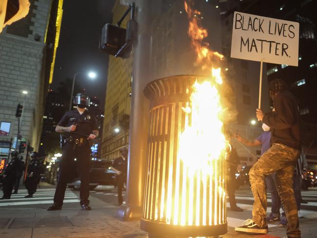 A protester holding a sign standing next to a burning trash can during a protest over the death of George Floyd in Los Angeles. Picture: AP