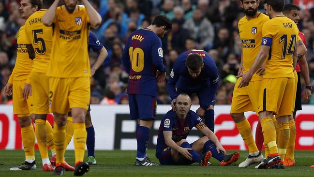 FC Barcelona's Andres Iniesta, center, sits on the pitch after being injured