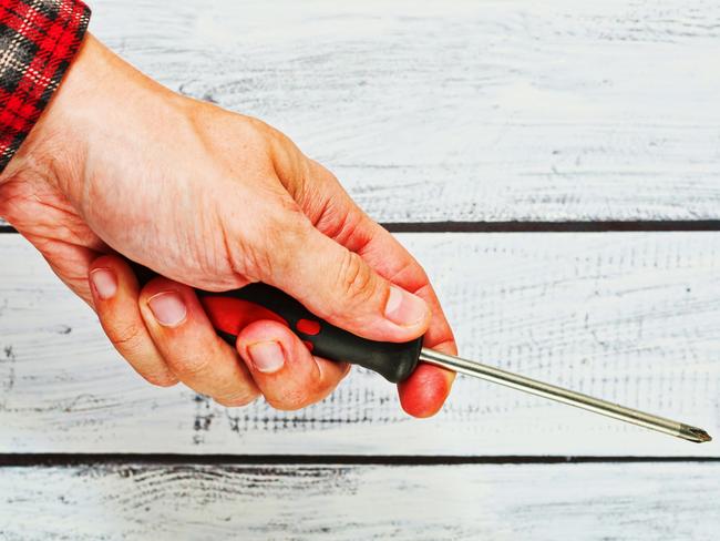 Screwdriver, generic, man. Handyman wearing a classic work shirt is holding a screwdriver in his hand. part of the body only, unrecognizable person with rough skin. Close-up capture.