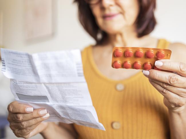 Close up of a Latin woman using medicine pills. She is sitting on bed and reading patient information leaflet.