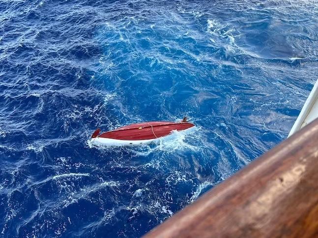 Tom Robinson hangs off the side of his overturned boat as a passenger cruise ship comes to his rescue. Picture: Supplied