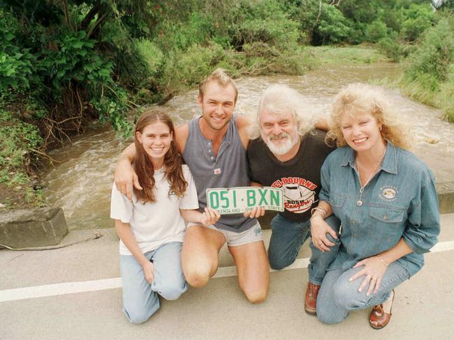1999: Brian Cadd holding car numberplate, with Linda Newman and her daughter Lauren at the bridge where their car was swept into the Bonogin Creek on the Gold Coast where they were rescued by local resident David Stubbs.