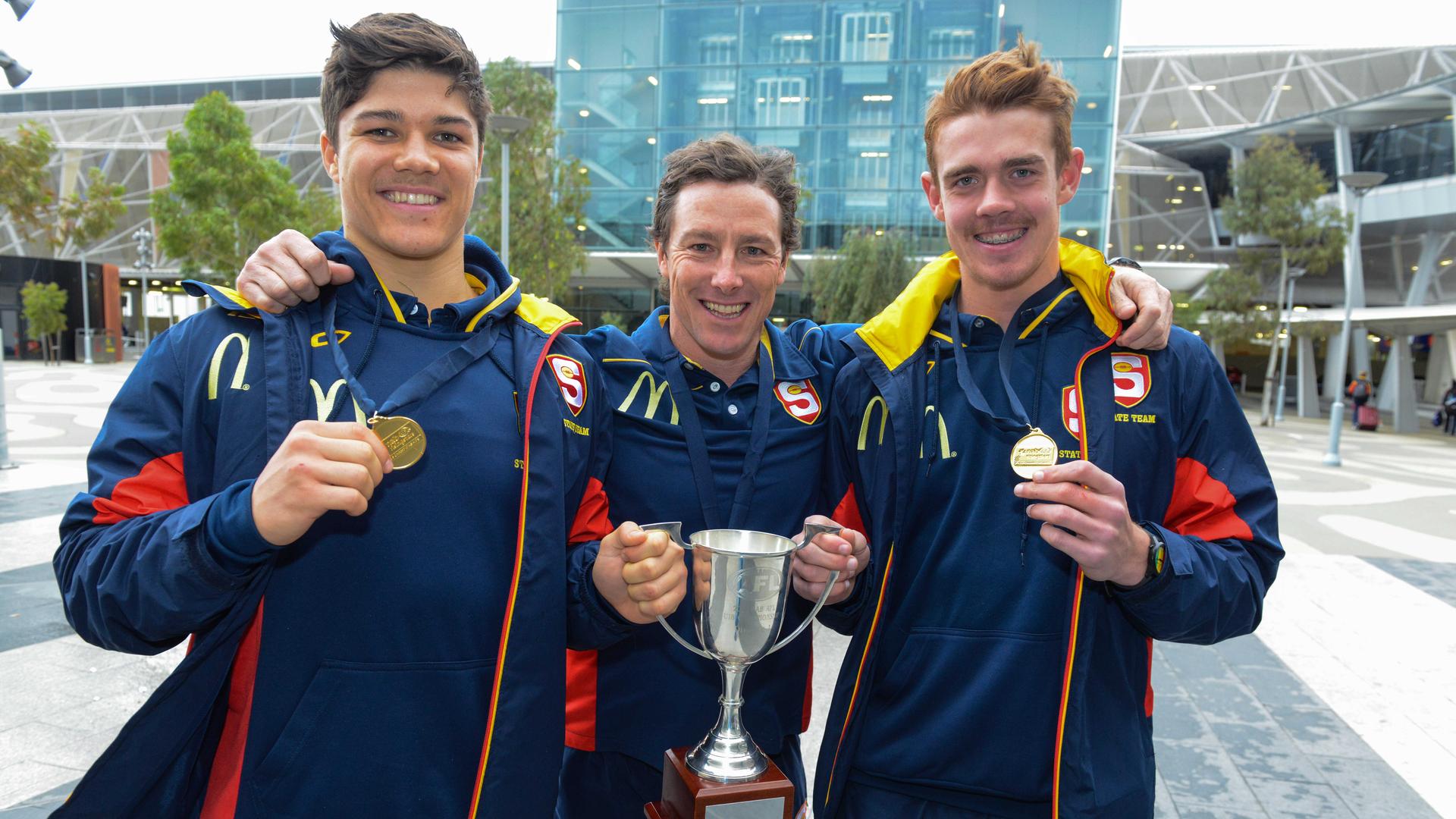 SA U18 championship football coach Tony Bamford and players Tom Lewis and Jez McLennan at Adelaide Airport with the trophy they won in Melbourne.