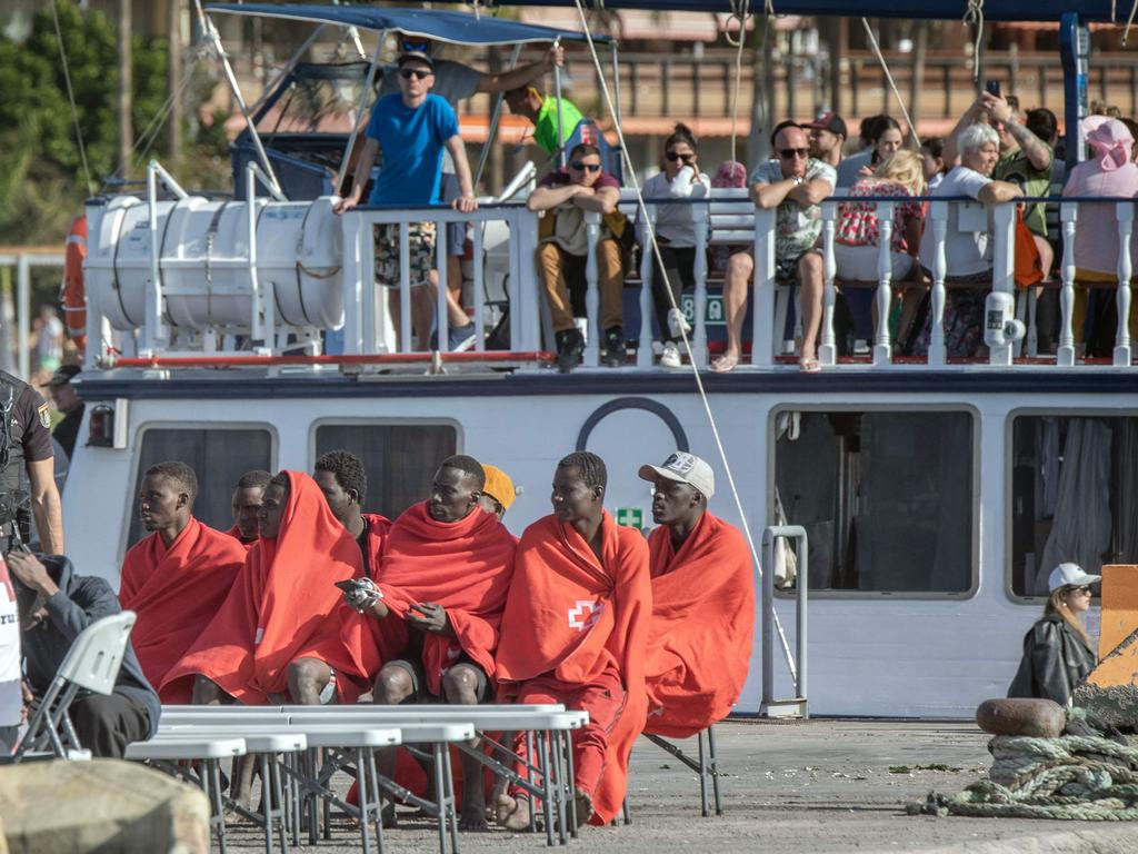 Tourists aboard a boat look at 41 migrants sitting on the pier of Los Cristianos port following their rescue by the Spanish Salvamento Maritimo in Tenerife. Picture: Desiree Martin/AFP