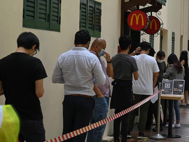 People wearing face masks as a prevention measure against the spread of the COVID-19 coronavirus queue outside a McDonald's fast food restaurant on its first day of opening after three weeks closure due to the pandemic in Singapore on May 11, 2020. (Photo by ROSLAN RAHMAN / AFP)