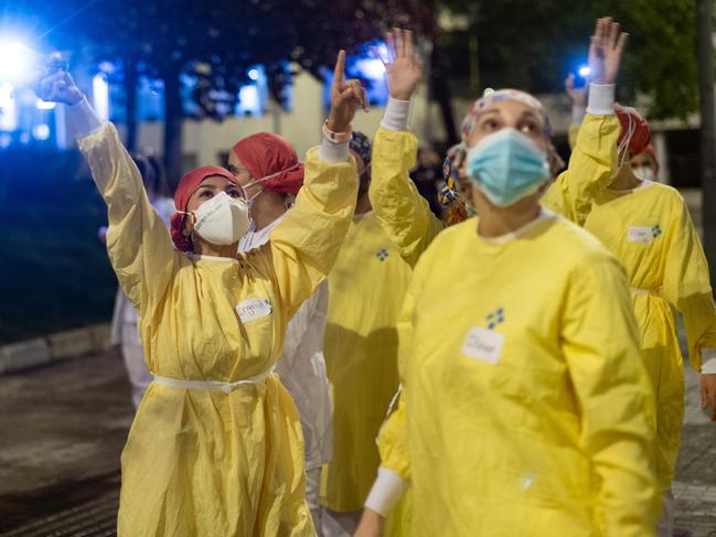 Healthcare workers wearing face masks and protective suits acknowledge applause outside the Hospital de Barcelona to people in his houses in Barcelona. Picture: AFP