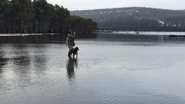 Charles Wooley's dog Dusty stands next to his new best friend trout fishing guide Greg Beecroft as he casts off in the snow-edged waters of a lake in the Central Plateau. Picture: Charles Wooley