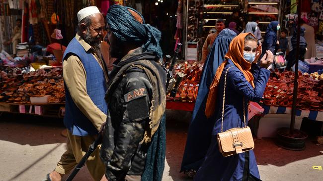 A Taliban fighter, centre, walks past shoppers along Mandawi market in Kabul on Wednesday. Picture: AFP)