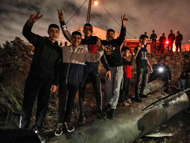 Palestinian youths celebrate as they stand atop a fallen projectile after Iran launched a barrage of missiles at Israel overnight. Picture: Zain JAAFAR / AFP