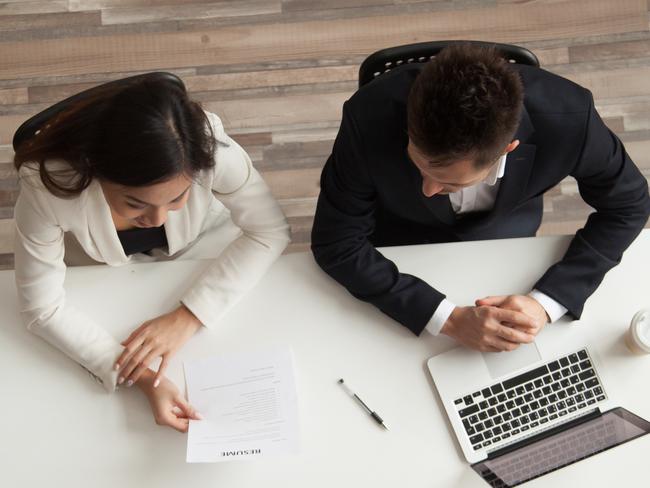 CAREERS: Female vacancy candidate answering questions at job interview talking to hr managers holding resume at office table, making good first impression, recruiting and hiring concept, top vertical view