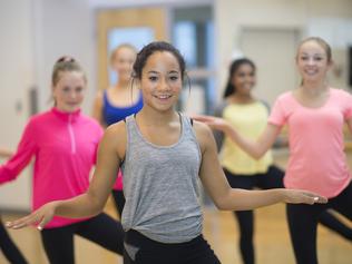 A multi-ethnic group of high school age girls are taking aerobic dance fitness class at the gym.