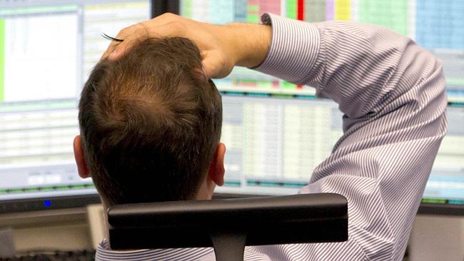  Rear view of a stock trade worker with his hand on his head watching the stock market on multiple computer screens in office...