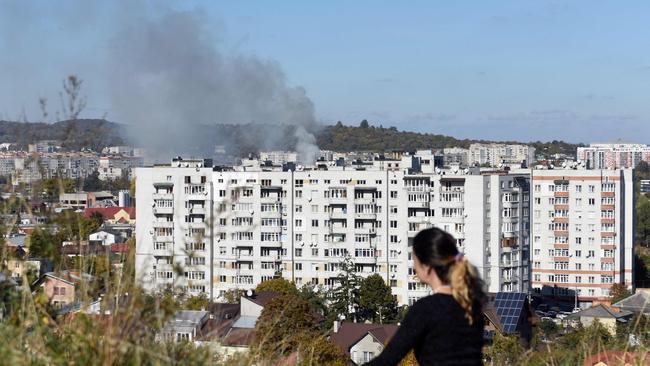 A woman sits on the hill as smoke rises above buildings in the western Ukrainian city of Lviv after an overnight (AEDT) Russian missile strike. Picture: AFP