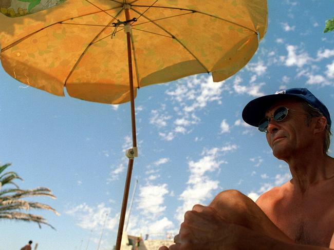 Mike Bignold with hat on & under umbrella in effort to avoid sun whilst at Cottesloe beach, WA./skin cancer/sunbathing/sunbaking