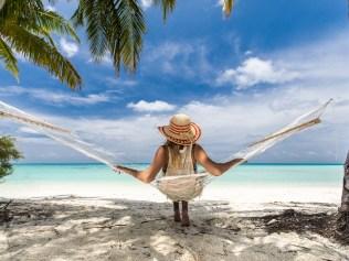 Back view of a woman with sun hat in hammock on the beach.