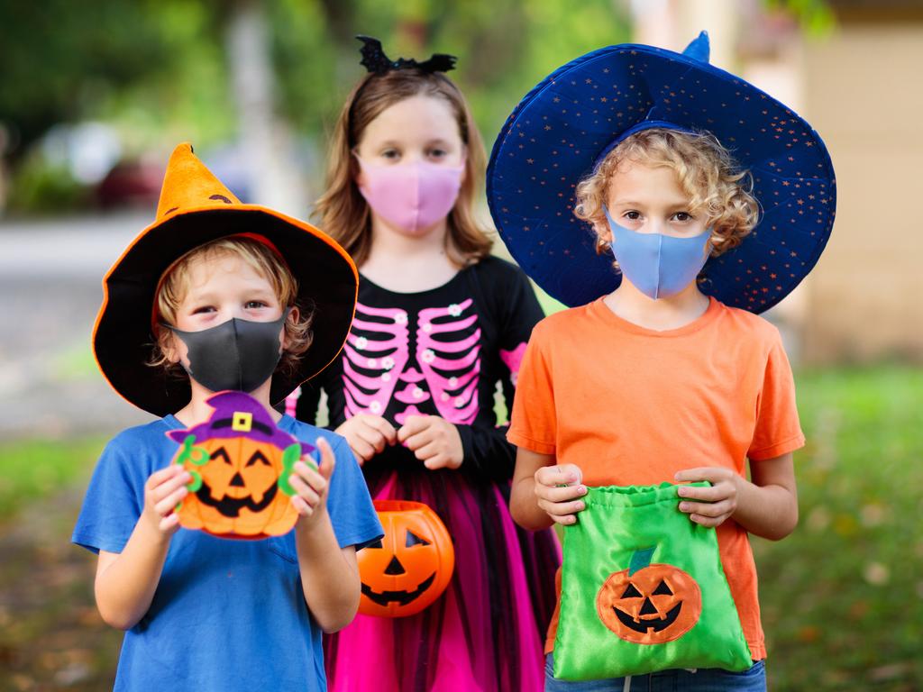 Kids trick or treat in Halloween costume and face mask. Children in dress up with candy bucket in coronavirus pandemic. Little boy and girl trick or treating with pumpkin lantern. Autumn holiday fun.