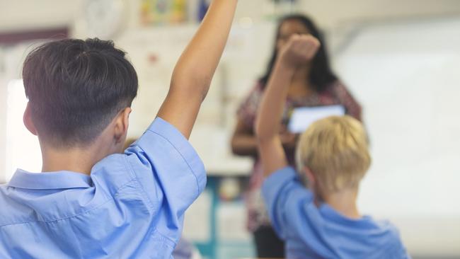 Aboriginal Elementary school teacher giving a presentation to the class. The students have their hands raised to ask questions in the classroom