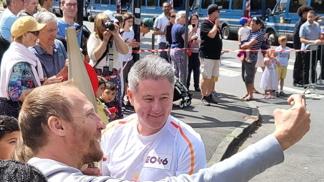 Mike Sneesby holds up the Olympic flame for a selfie.