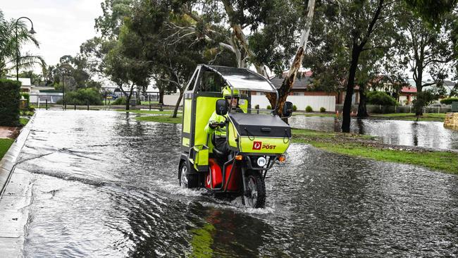 A postie delivers mail through flood water in Plympton from an overnight storm. Picture: NCA NewsWire / Brenton Edwards