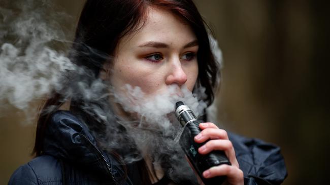 Vape teenager. Young pretty caucasian brunette girl smoking an electronic cigarette on the street in the spring. Deadly bad habit. i STOCK IMAGE