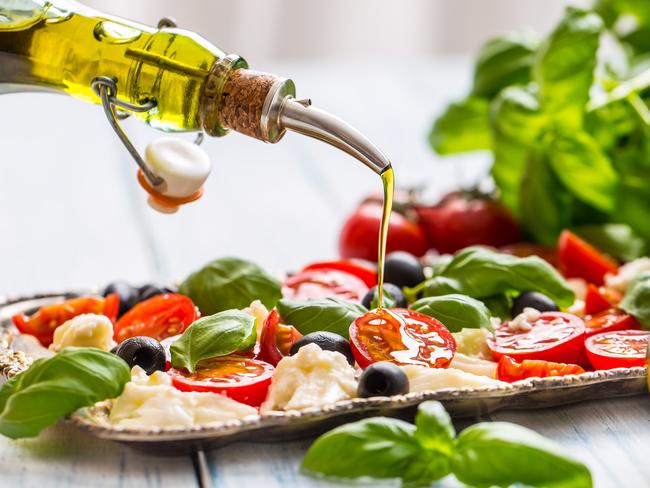 Pouring olive oil on caprese salad, which is a healthy Mediterranean meal.